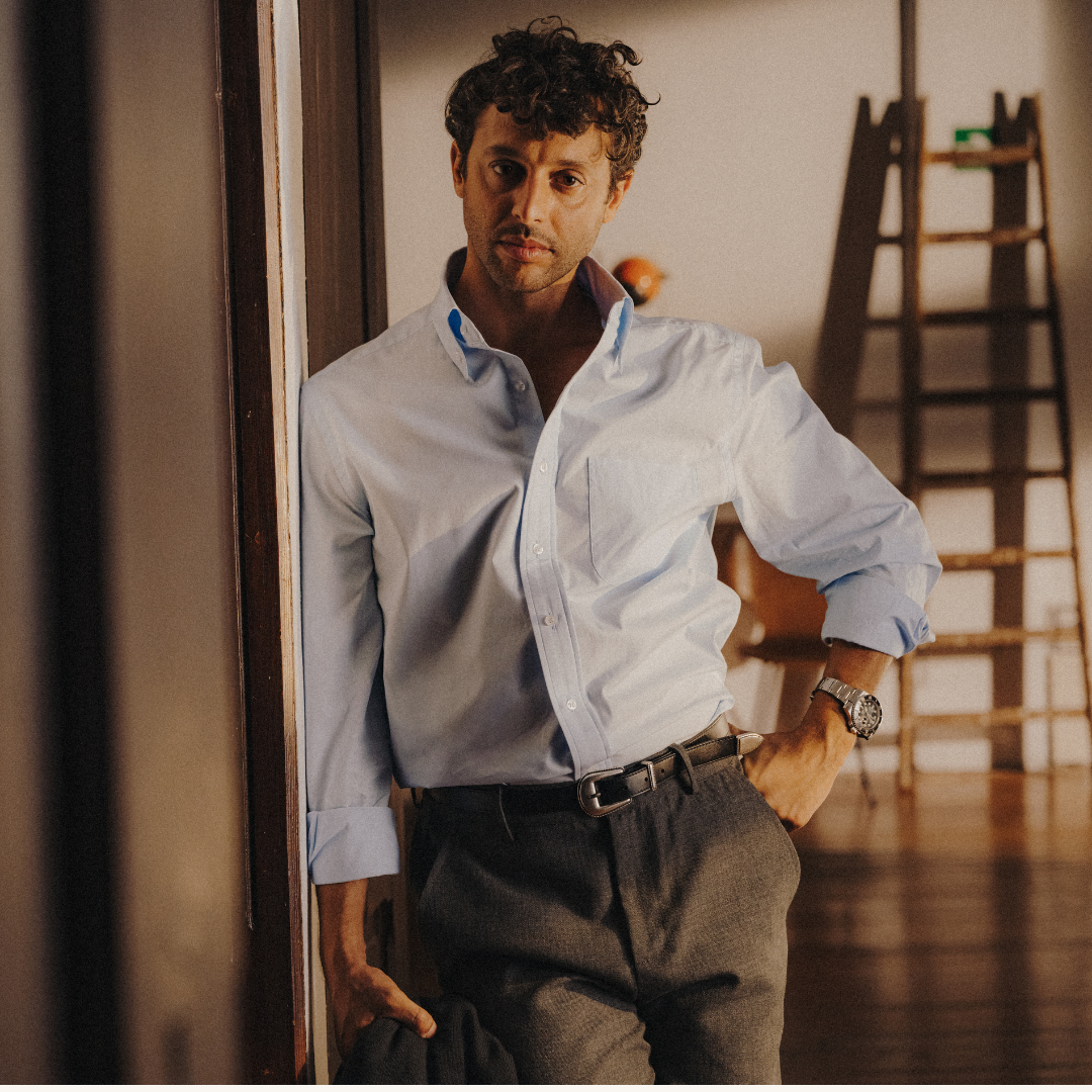 Man in a light blue shirt and dark pants standing in a room with wooden floors and a ladder.